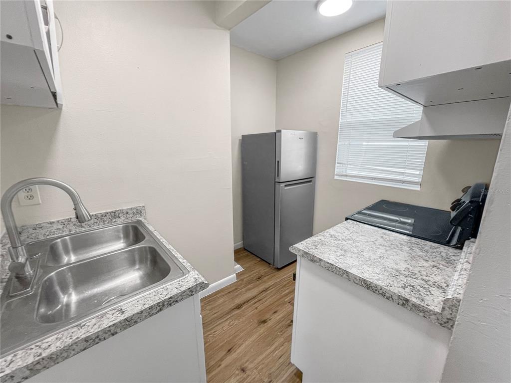 A small kitchen features stainless steel appliances, granite-look countertops, and light wood-style flooring — 321 W IANTHE STREET UNIT 6, TAVARES, FL