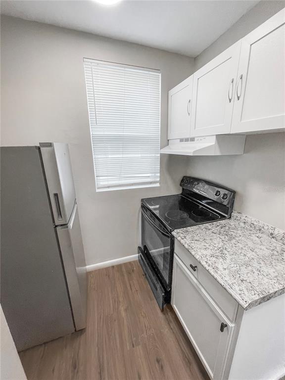 A small kitchen features white cabinets, granite countertops, a black stove, and a stainless refrigerator — 321 W IANTHE STREET UNIT 6, TAVARES, FL