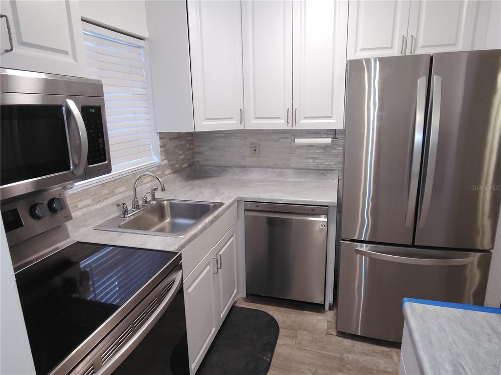A kitchen features white cabinets, stainless steel appliances, a sink, and gray countertops — 5955 PALM LANE UNIT A33, BRADENTON, FL