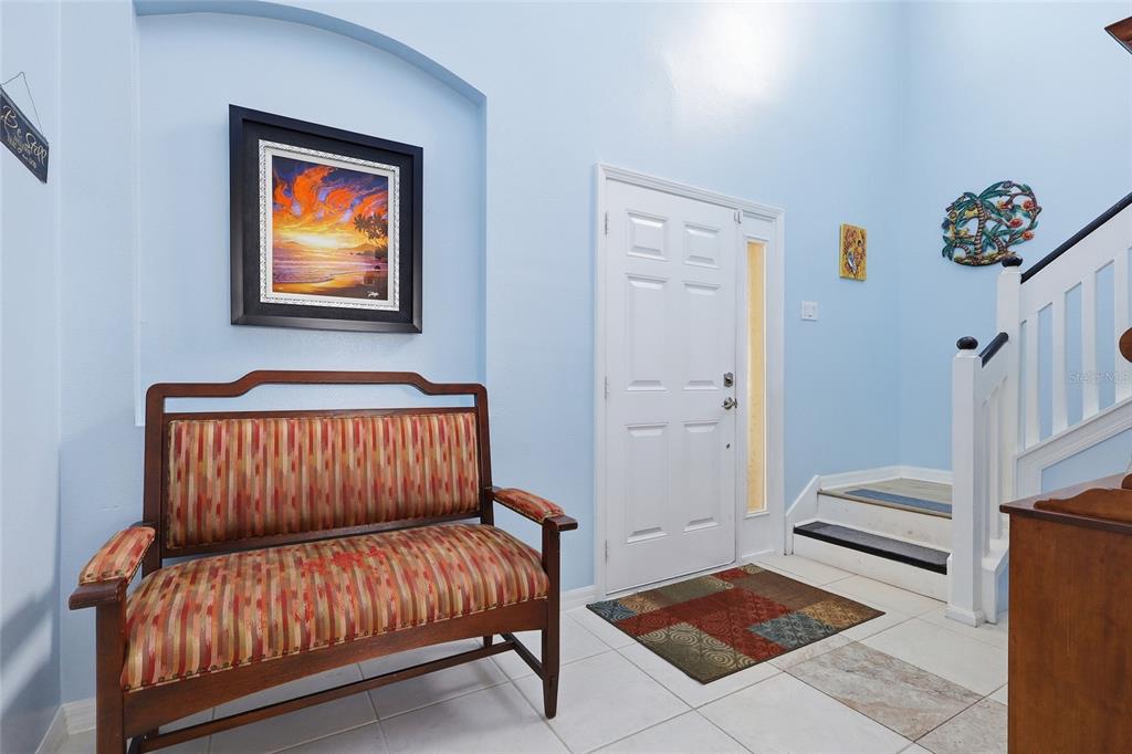 An entryway features a wooden bench, a framed sunset painting, and stairs with white railings — 7902 CARRIAGE POINTE DR, GIBSONTON, FL