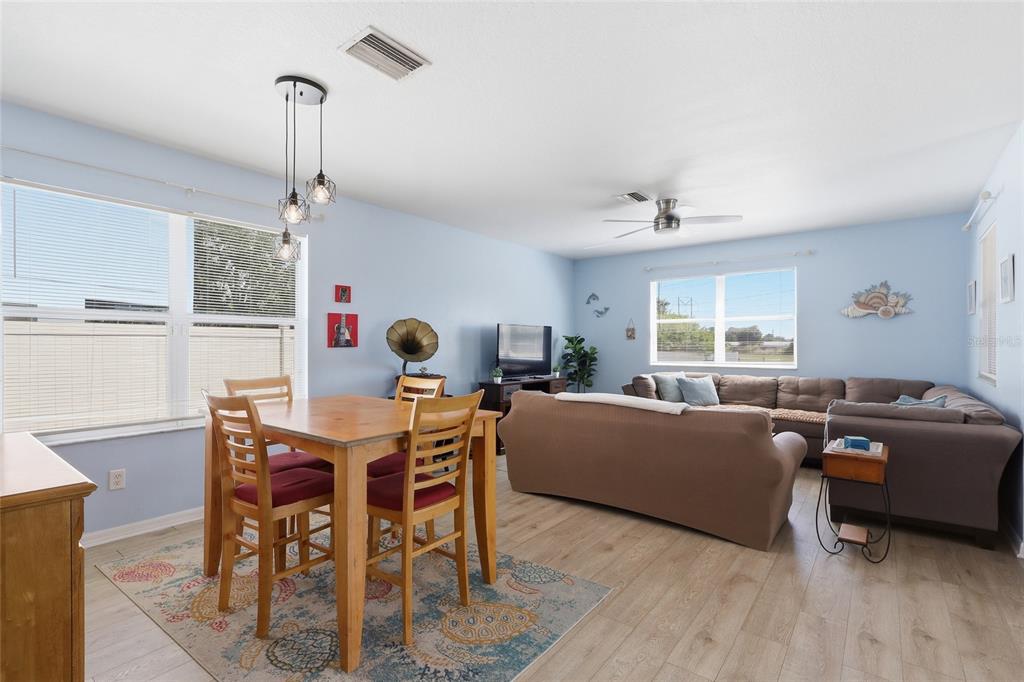 A living and dining area with light blue walls, wood-look flooring, and a sectional sofa — 7902 CARRIAGE POINTE DR, GIBSONTON, FL