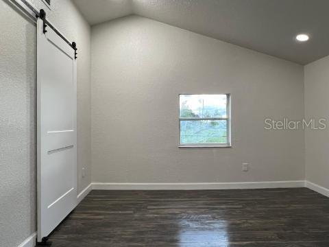 A room with dark wood-look flooring, white walls, a vaulted ceiling, and a sliding barn door — 1526 LAKEWOOD ROAD, DAVENPORT, FL