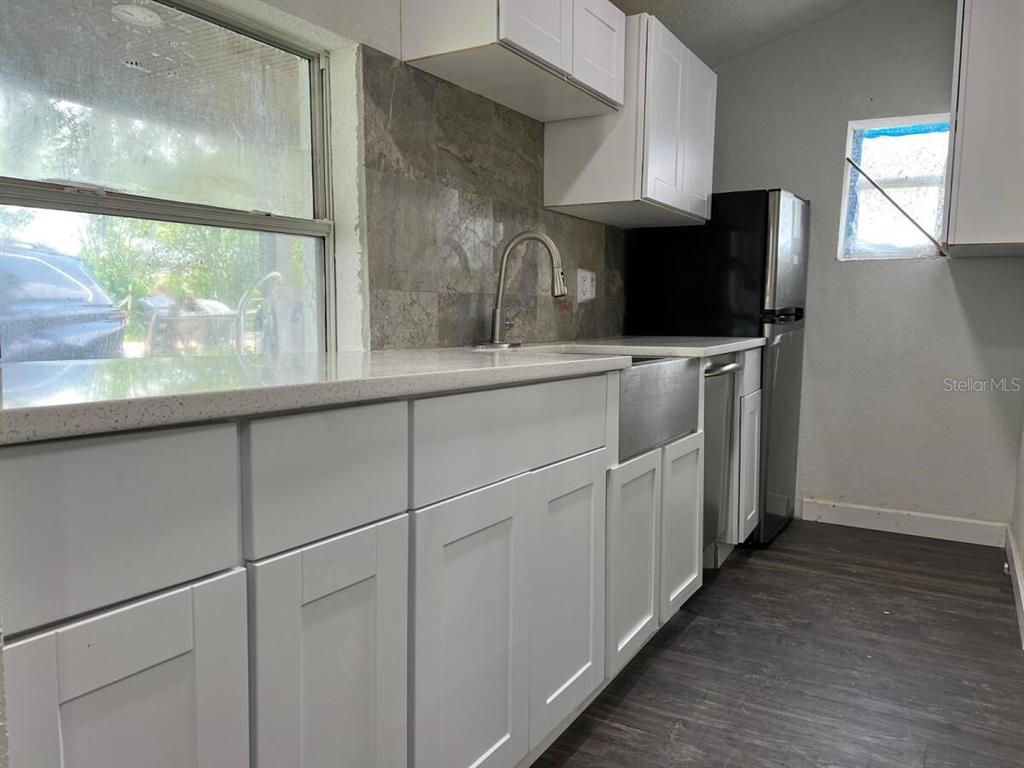 A kitchen features white cabinets, a farmhouse sink, a tiled backsplash, and stainless steel appliances — 1526 LAKEWOOD ROAD, DAVENPORT, FL