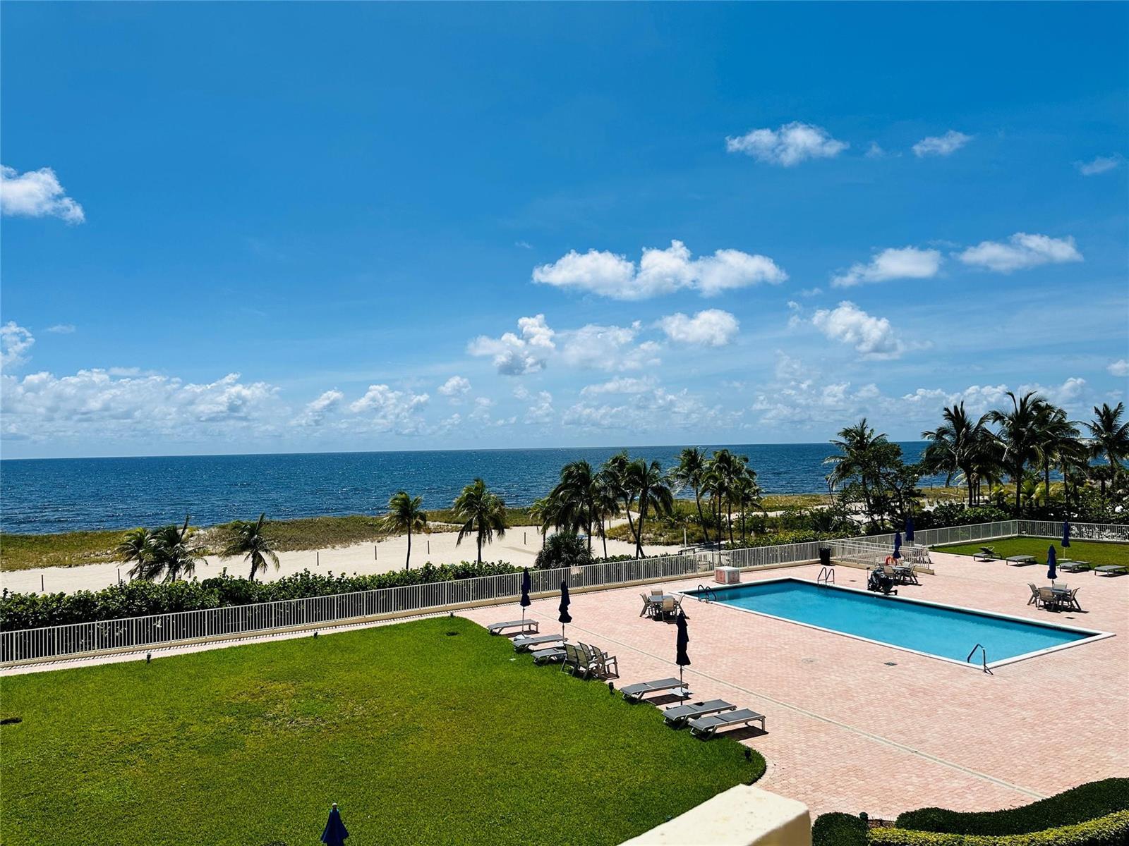 An elevated view of a swimming pool, lawn, and sandy beach overlooking the ocean — 750 N Ocean Boulevard # 404, Pompano Beach FL 33062, POMPANO BEACH, FL