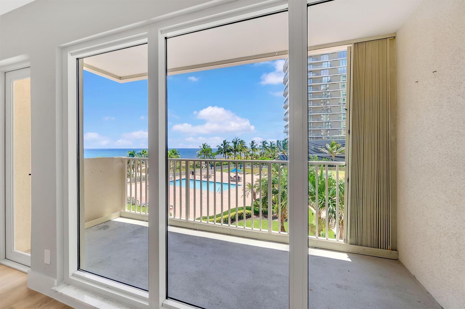 A balcony with a white railing overlooks a swimming pool, palm trees, and the ocean — 750 N Ocean Boulevard # 404, Pompano Beach FL 33062, POMPANO BEACH, FL