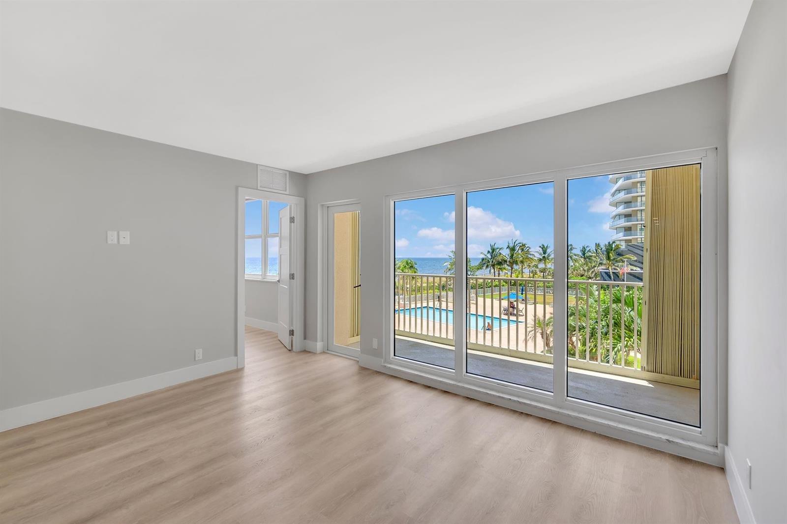 An empty room with light wood flooring, gray walls, and a balcony overlooking a pool — 750 N Ocean Boulevard # 404, Pompano Beach FL 33062, POMPANO BEACH, FL