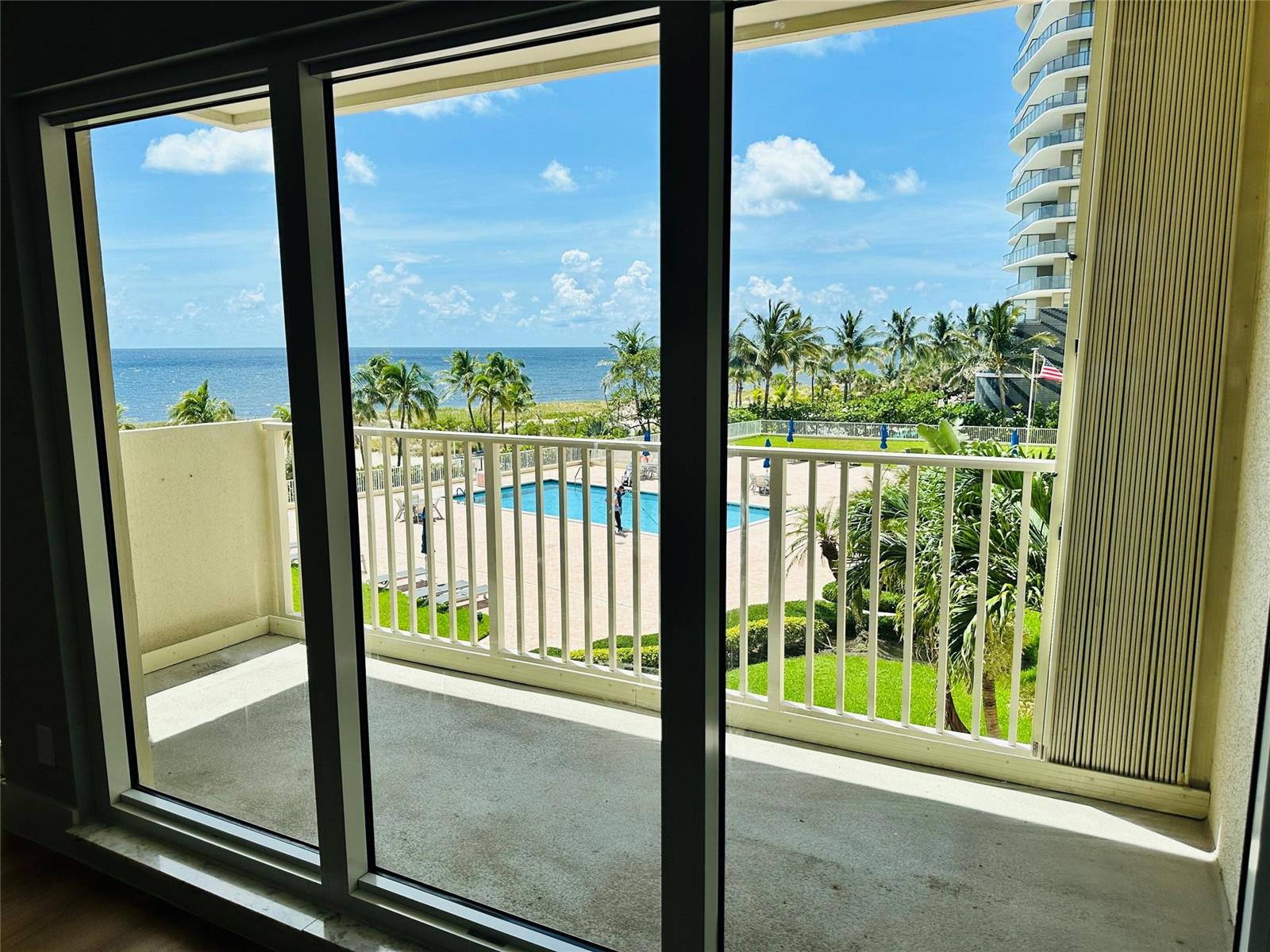 A balcony view overlooking a swimming pool, palm trees, and the ocean — 750 N Ocean Boulevard # 404, Pompano Beach FL 33062, POMPANO BEACH, FL