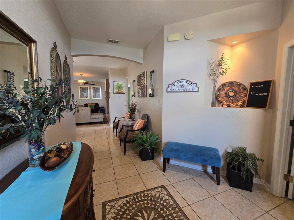 A tiled entryway features a blue bench, wall decor, and a view into the living room — 219 CLOVERDALE ROAD, WINTER HAVEN, FL