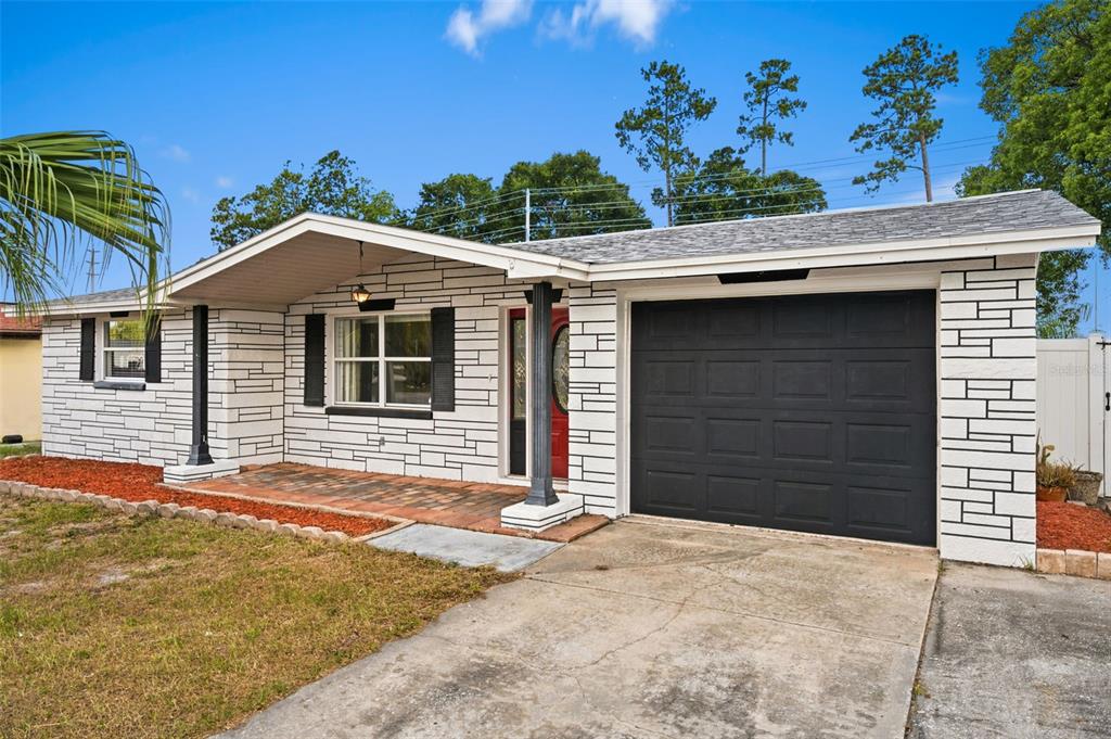 A single-story house with white stone-patterned siding, a black garage door, and a front porch — 5753 1ST AVENUE, NEW PORT RICHEY, FL