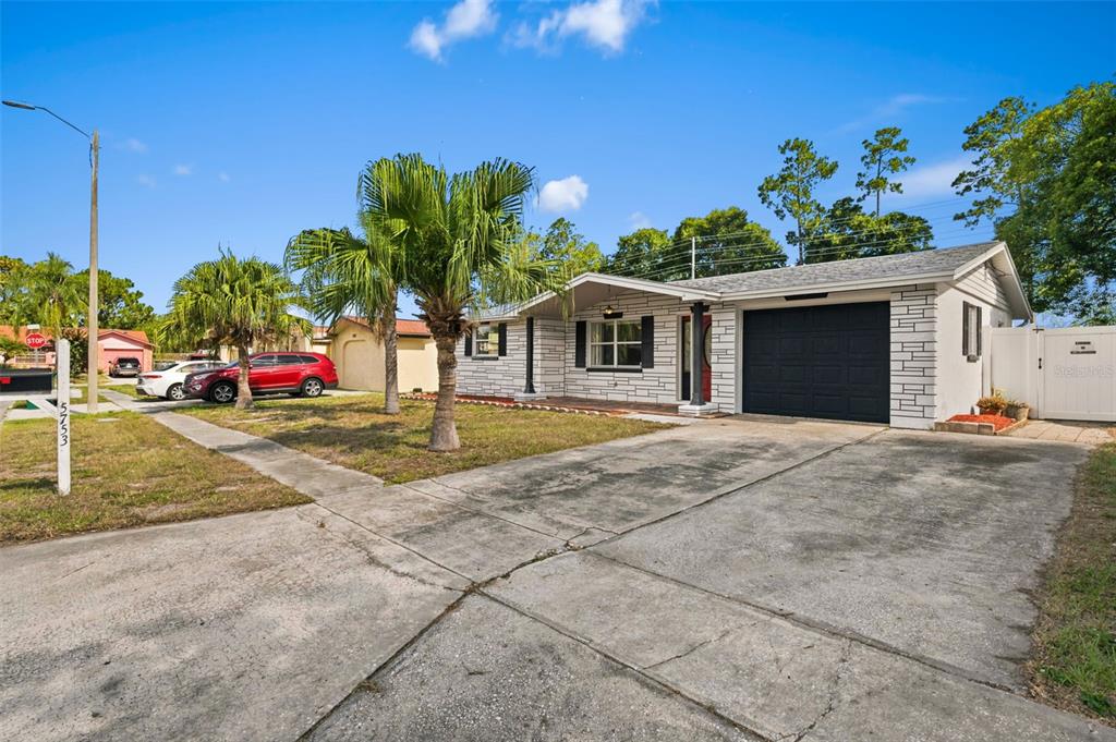 A single-story house with a white stone facade, black garage door, and palm trees — 5753 1ST AVENUE, NEW PORT RICHEY, FL