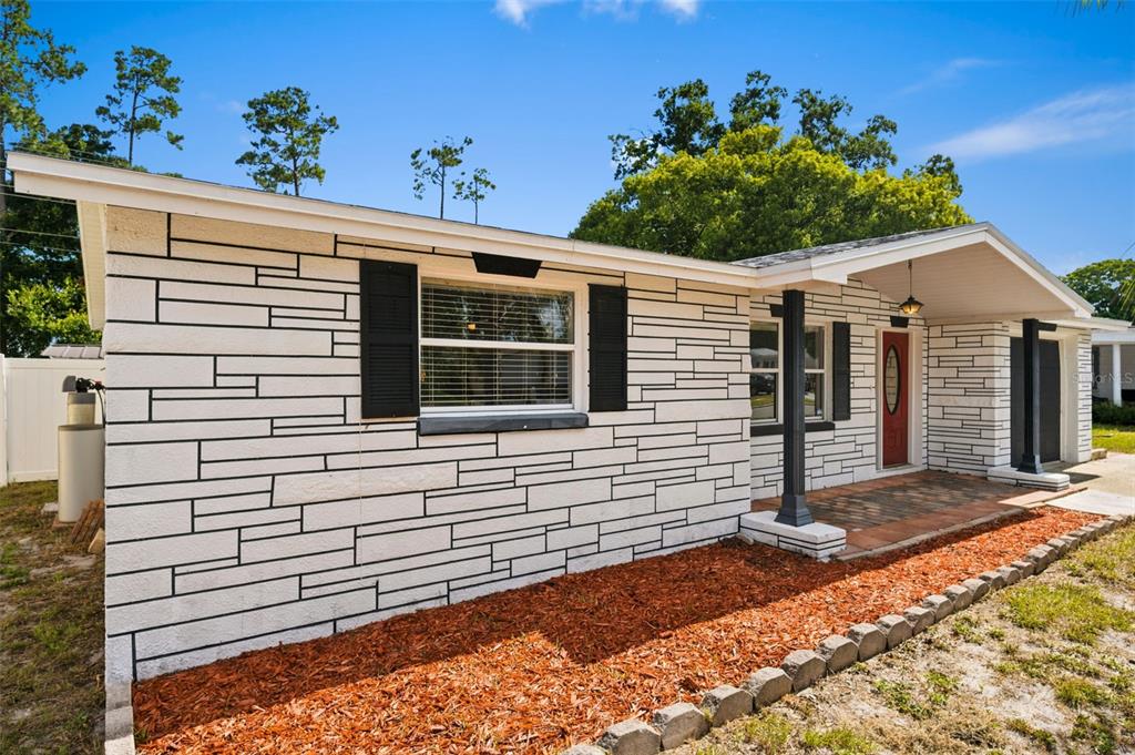 A single-story house exterior features white stone-patterned siding, a red front door, and mulch landscaping — 5753 1ST AVENUE, NEW PORT RICHEY, FL