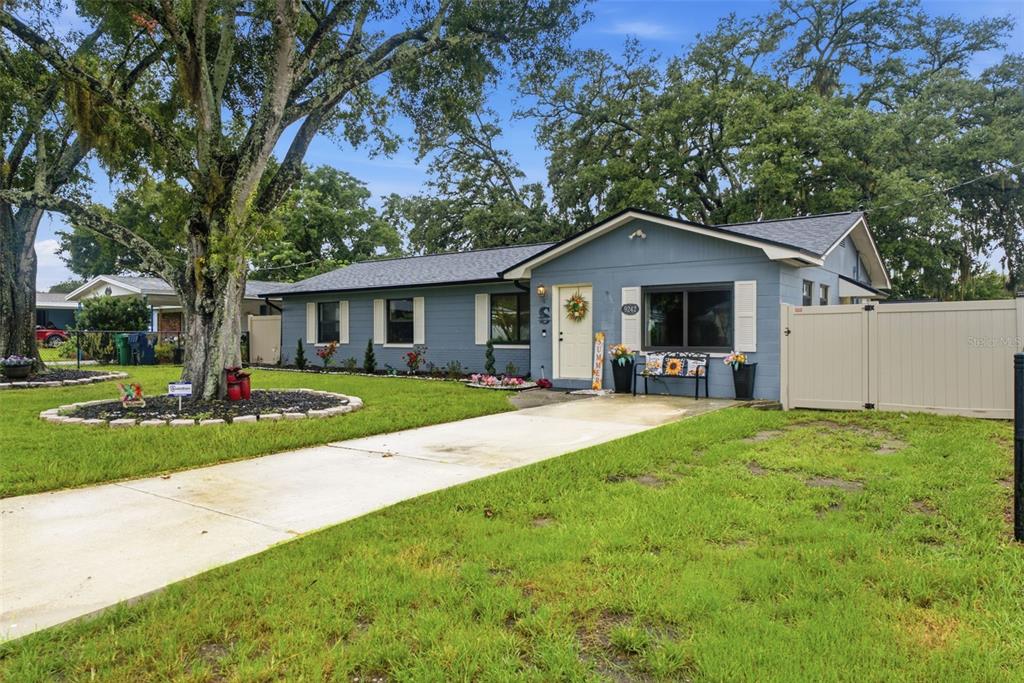 A blue single-story house with a white front door, concrete driveway, and large oak trees — 9242 N 52ND STREET, TAMPA, FL