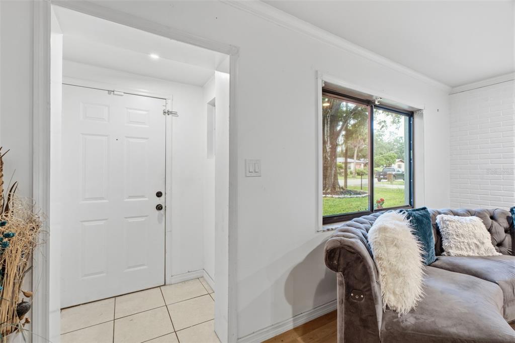 A white front door opens into a tiled entryway next to a living room with furniture — 9242 N 52ND STREET, TAMPA, FL