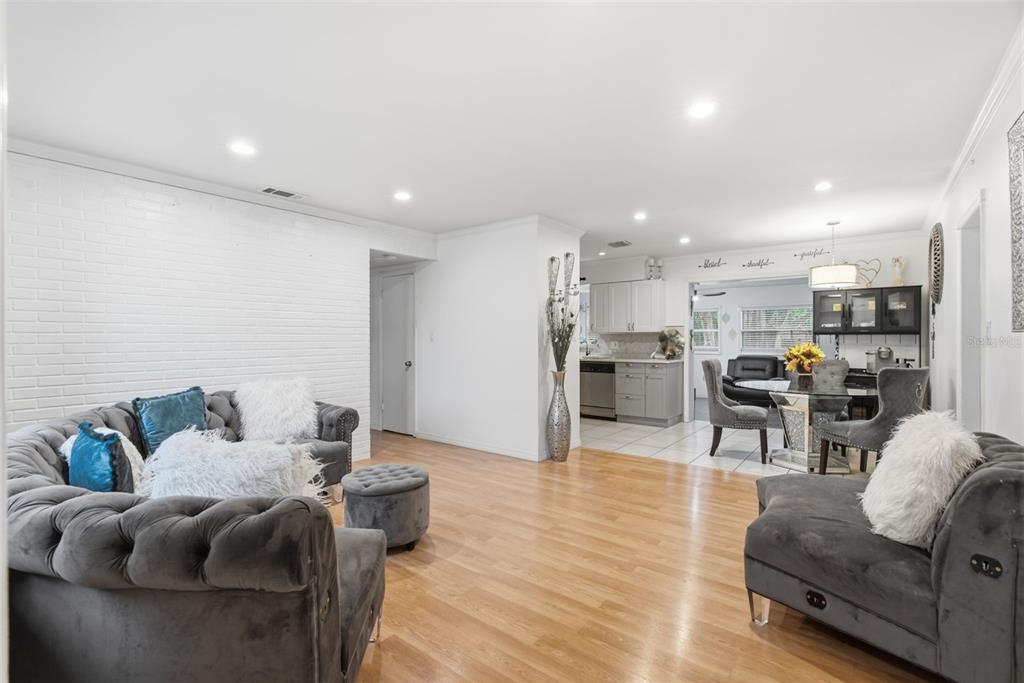 A living room with a white brick wall, gray tufted furniture, and an adjacent kitchen — 9242 N 52ND STREET, TAMPA, FL