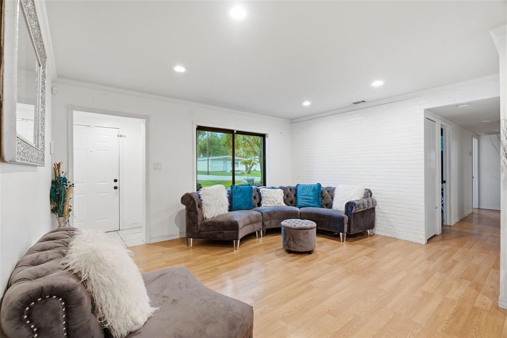 A living room features light wood flooring, a white brick wall, and gray tufted furniture — 9242 N 52ND STREET, TAMPA, FL