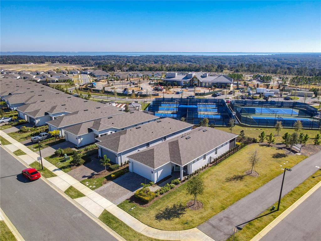 An aerial view shows a residential street with modern townhomes, tennis courts, and a clubhouse — 2750 PURPLE MEADOW COURT, MINNEOLA, FL