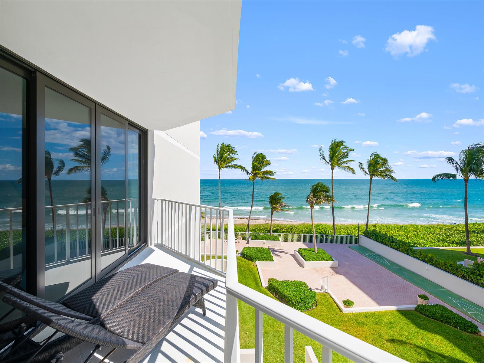 A balcony with lounge chairs overlooks a grassy lawn, palm trees, and the ocean — 2917 S Ocean Boulevard # 304, Highland Beach FL 33487, HIGHLAND BEACH, FL