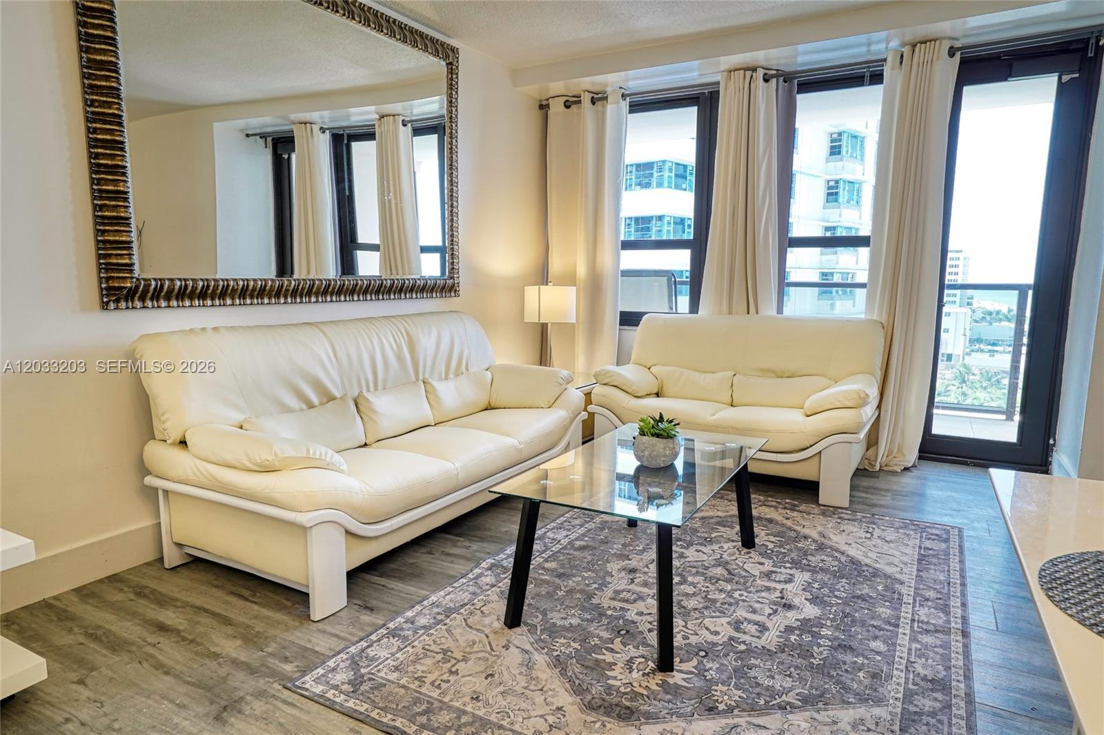 A living room features two cream-colored sofas, a glass coffee table, and a large mirror — 5225 Collins Ave # 1204, Miami Beach FL 33140, MIAMI BEACH, FL