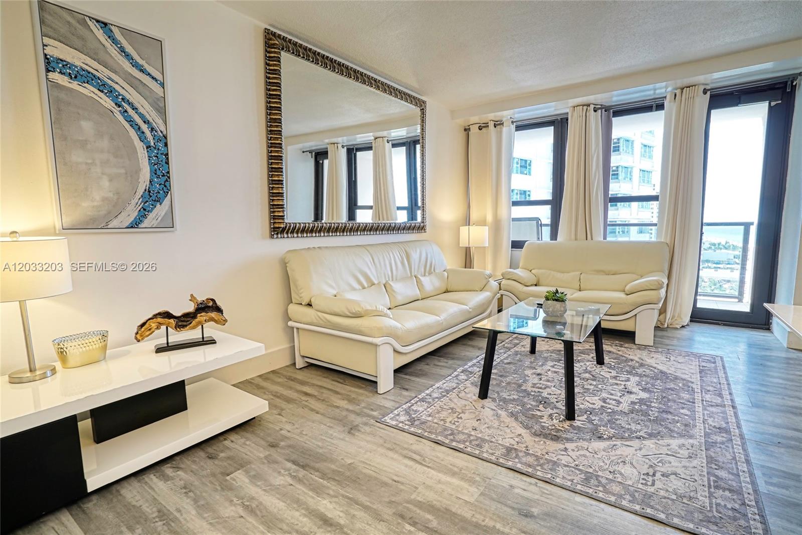 A living room features two cream-colored sofas, a glass coffee table, and a large mirror — 5225 Collins Ave # 1204, Miami Beach FL 33140, MIAMI BEACH, FL