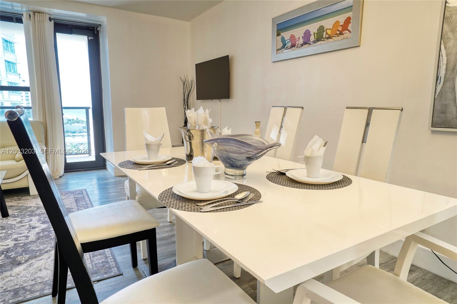 A dining room features a white table, modern chairs, and a view of the ocean — 5225 Collins Ave # 1204, Miami Beach FL 33140, MIAMI BEACH, FL