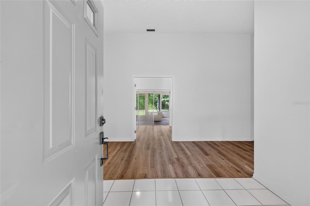An entryway with white tile floors transitions into a living area with wood-look flooring — 11 WALNUT PLACE, PALM COAST, FL