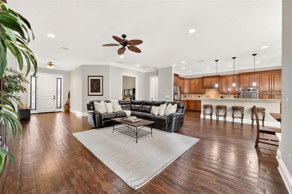 An open-concept living room and kitchen featuring dark wood floors, a sectional sofa, and cabinetry — 11050 SE 37TH AVENUE ROAD, BELLEVIEW, FL