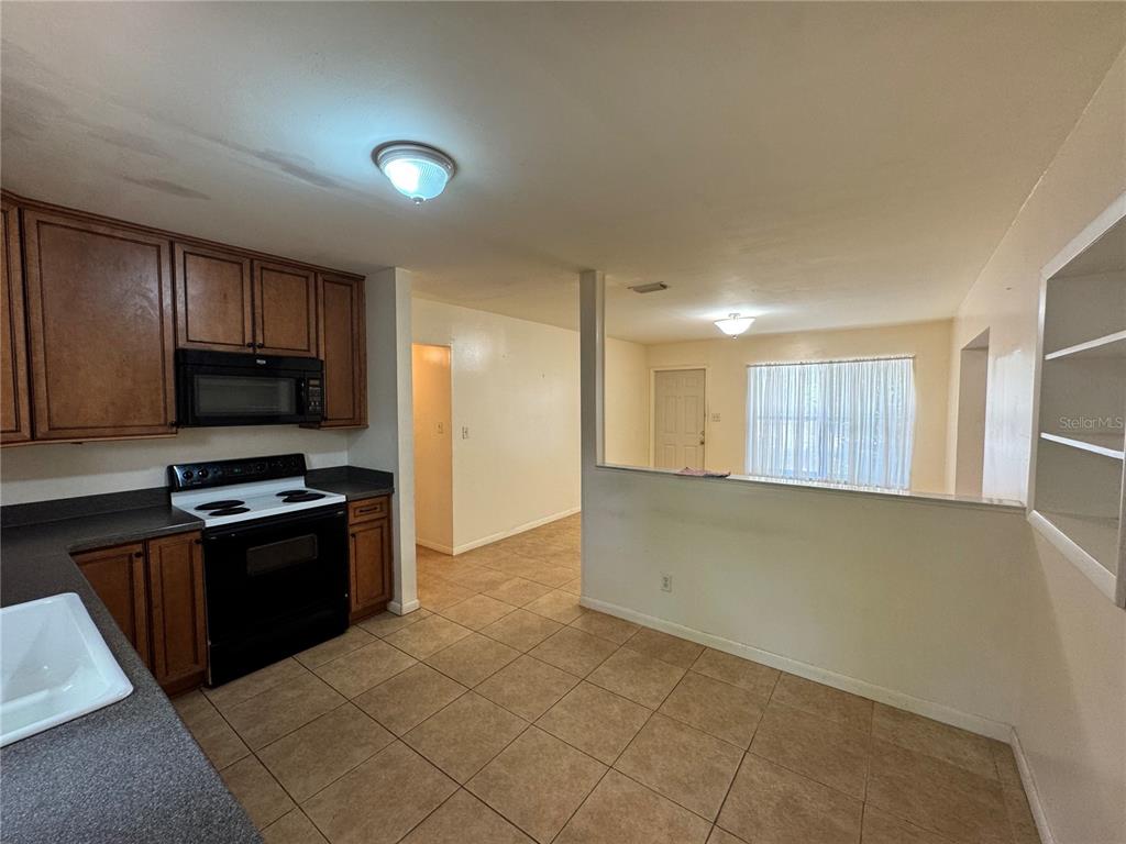 A kitchen with wooden cabinets, a black stove, and tile flooring opens to a living area — 3608 W LEILA AVENUE, TAMPA, FL