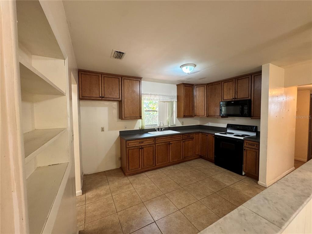 A kitchen with wood cabinets, dark countertops, tile flooring, and a white sink — 3608 W LEILA AVENUE, TAMPA, FL