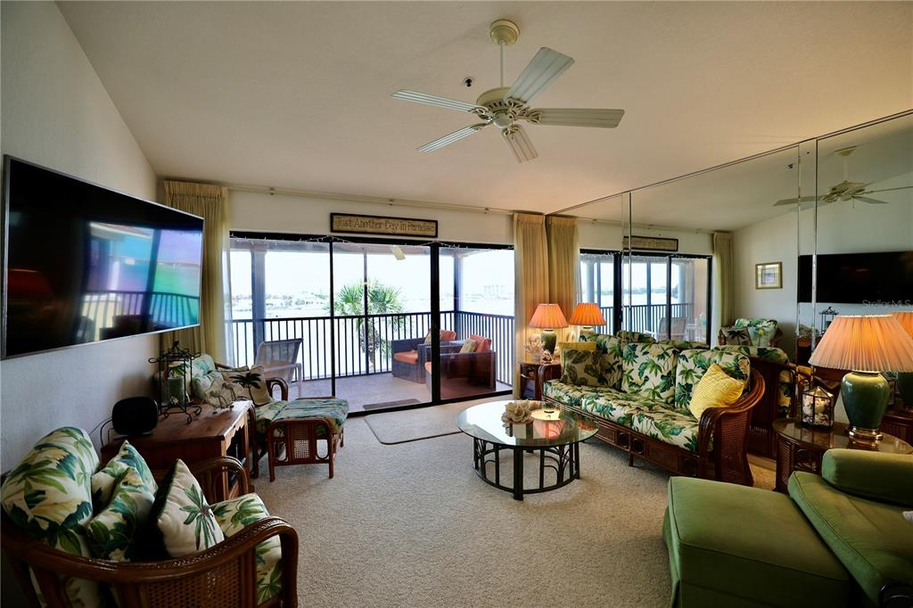 A living room features a tropical-patterned sofa, a glass coffee table, and a balcony view — 442 BOUCHELLE DRIVE UNIT 305, NEW SMYRNA BEACH, FL