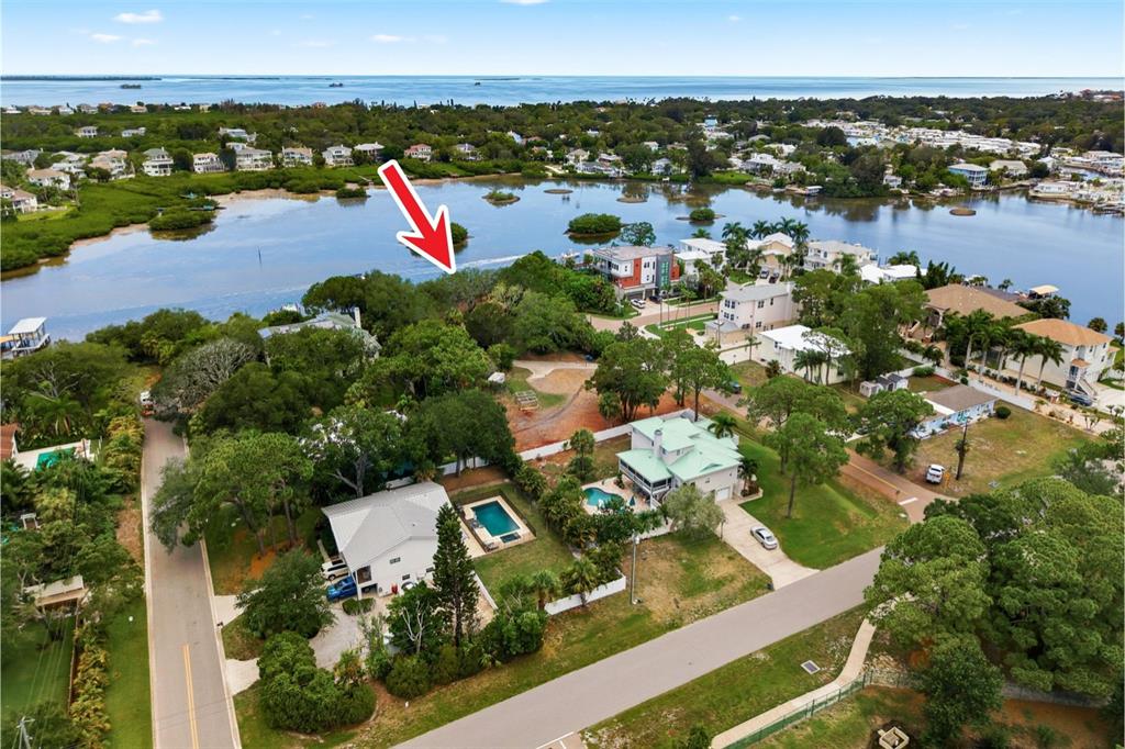 An aerial view shows a waterfront residential lot with trees near a bay and houses — 700 DELAWARE AVENUE, PALM HARBOR, FL