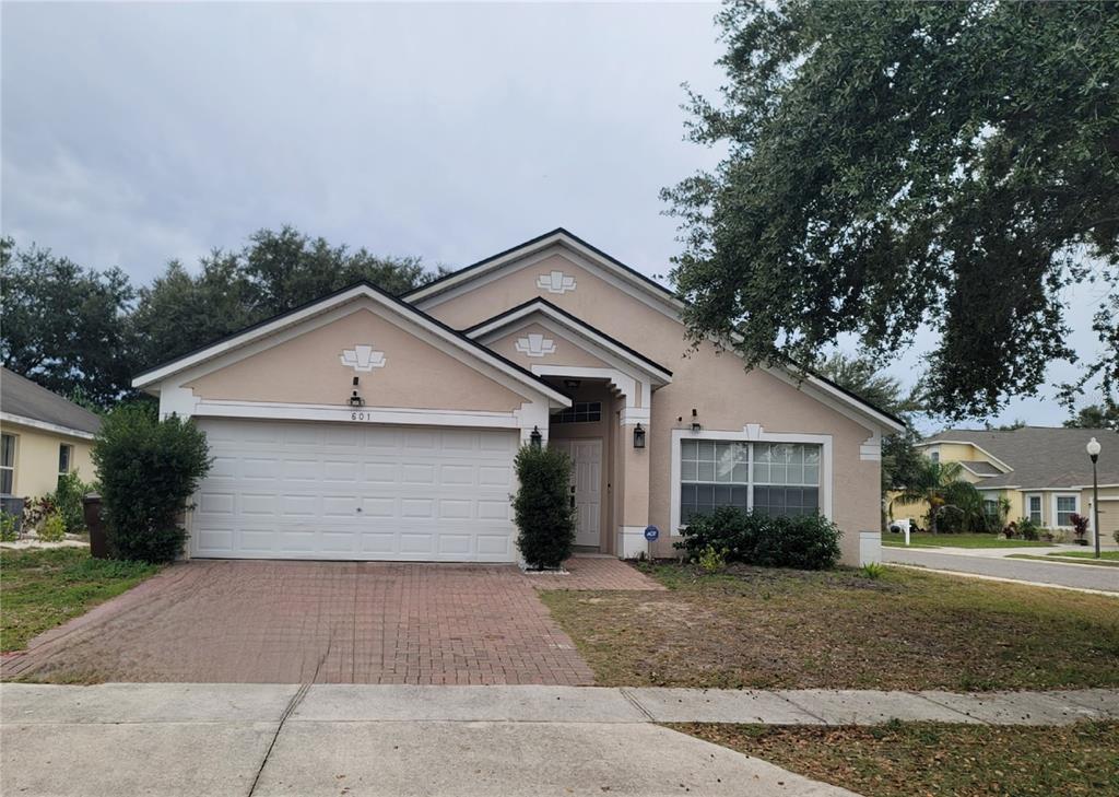A single-story house with a beige stucco exterior, a two-car garage, and a brick driveway — 601 ASTOR DRIVE, HAINES CITY, FL