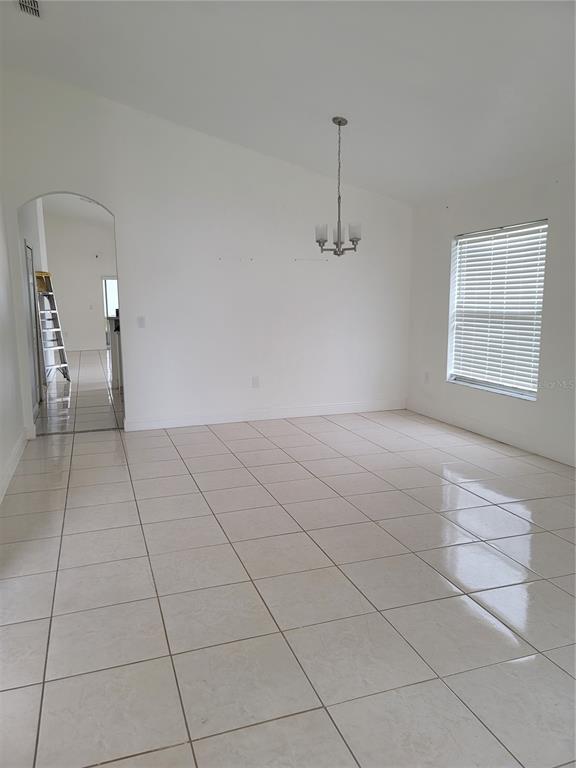 An empty dining room features white walls, tile flooring, a chandelier, and an arched doorway — 601 ASTOR DRIVE, HAINES CITY, FL