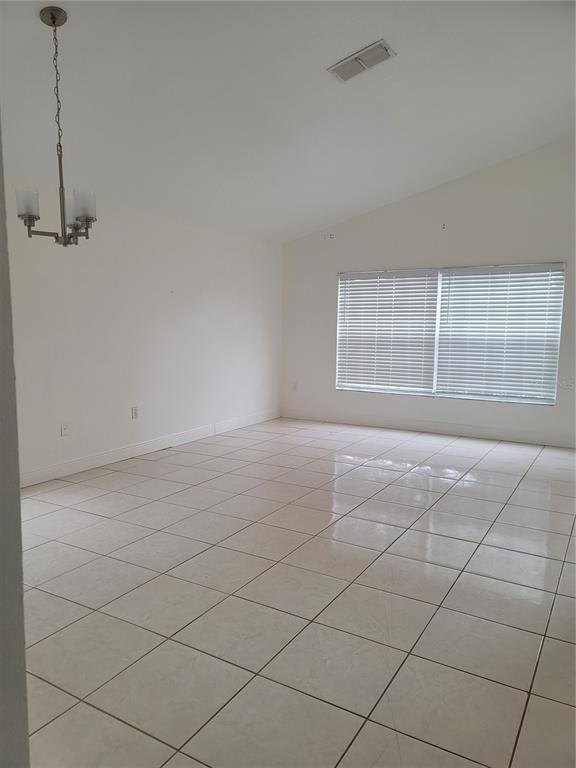 An empty dining room features white walls, a vaulted ceiling, a chandelier, and tiled flooring — 601 ASTOR DRIVE, HAINES CITY, FL