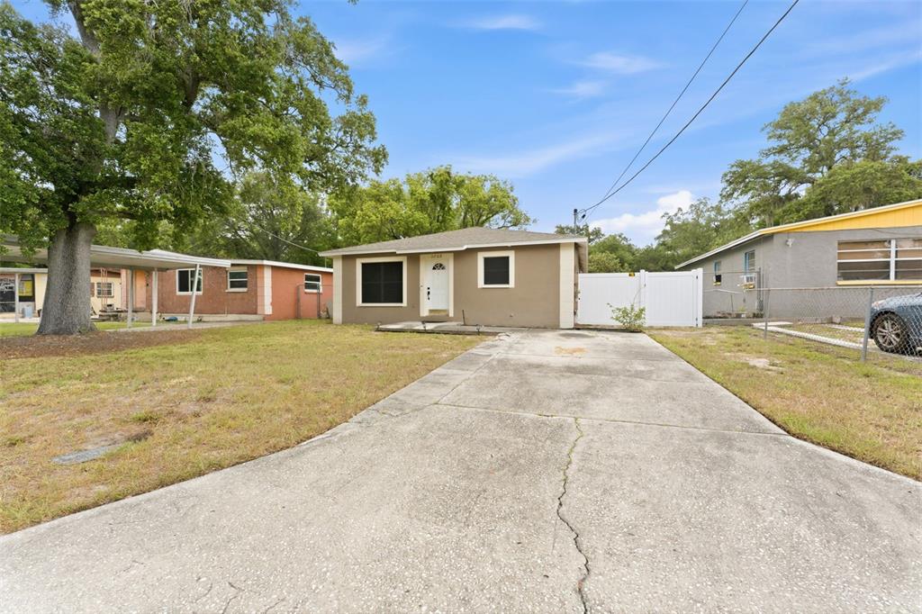 A single-story house with a concrete driveway, tan exterior, and a white fence — 3708 E IDLEWILD AVENUE, TAMPA, FL