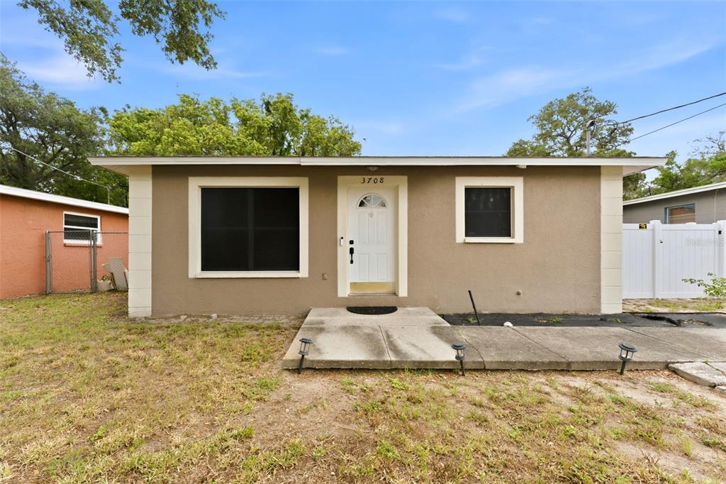 A single-story house with a tan exterior, white trim, and a concrete front walkway — 3708 E IDLEWILD AVENUE, TAMPA, FL