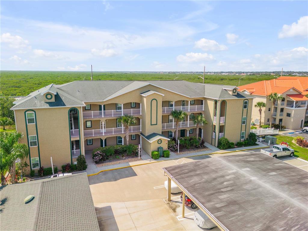 An aerial view of a three-story apartment building with a parking lot and carport — 468 BOUCHELLE DRIVE UNIT 325, NEW SMYRNA BEACH, FL