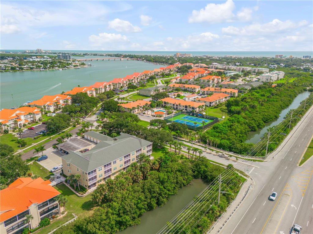 An aerial view shows a residential complex with orange-roofed buildings, tennis courts, and nearby water — 468 BOUCHELLE DRIVE UNIT 325, NEW SMYRNA BEACH, FL