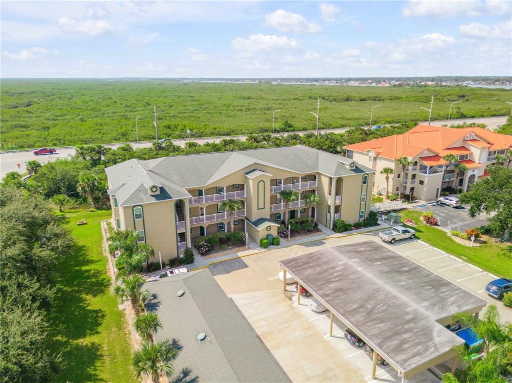 An aerial view shows a multi-story apartment building with a parking lot and covered carports — 468 BOUCHELLE DRIVE UNIT 325, NEW SMYRNA BEACH, FL