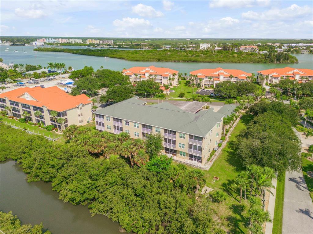 An aerial view shows a multi-story apartment building surrounded by lush trees and a waterway — 468 BOUCHELLE DRIVE UNIT 325, NEW SMYRNA BEACH, FL