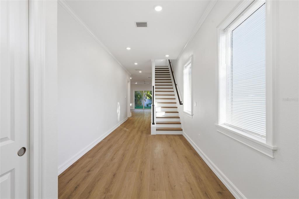 A hallway with light wood flooring leads to a staircase and a view of greenery — 3809 71ST STREET N, ST PETERSBURG, FL