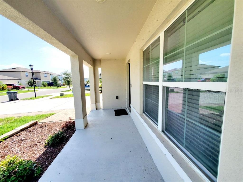 A covered concrete front porch features a large window and a view of the street — 1014 GOLDEN SHINER AVENUE, RUSKIN, FL