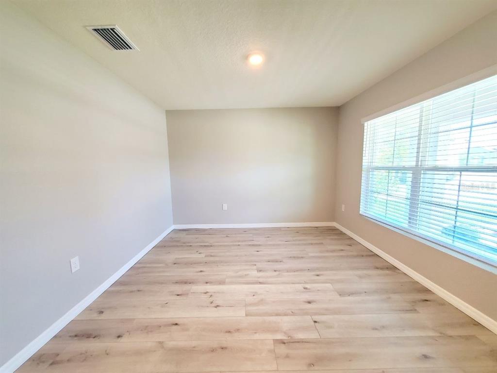 An empty room with light-colored walls, wood-look flooring, and a large window with blinds — 1014 GOLDEN SHINER AVENUE, RUSKIN, FL