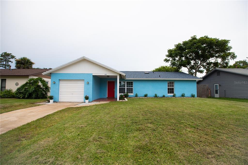 A single-story house with bright blue brick siding, a white garage door, and a red door — 526 DORSET CIRCLE, SOUTH DAYTONA, FL
