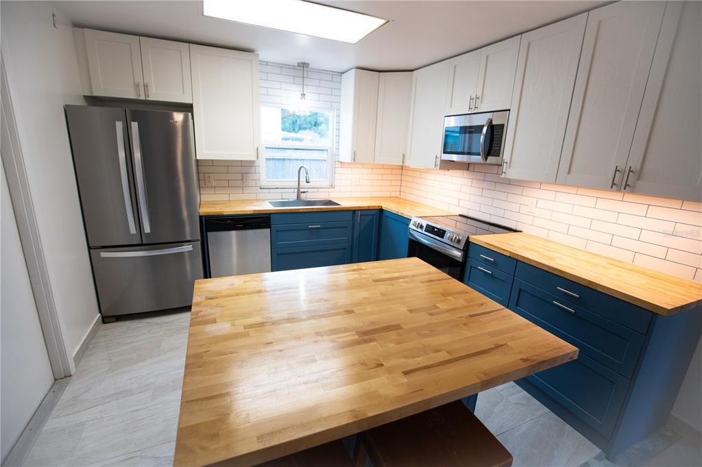A kitchen features blue lower cabinets, white upper cabinets, butcher block countertops, and stainless appliances — 526 DORSET CIRCLE, SOUTH DAYTONA, FL