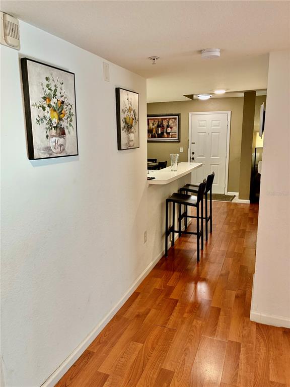 A hallway with wood flooring leads to a kitchen bar area with two stools — 4122 RESIDENCE DRIVE UNIT 120, FORT MYERS, FL