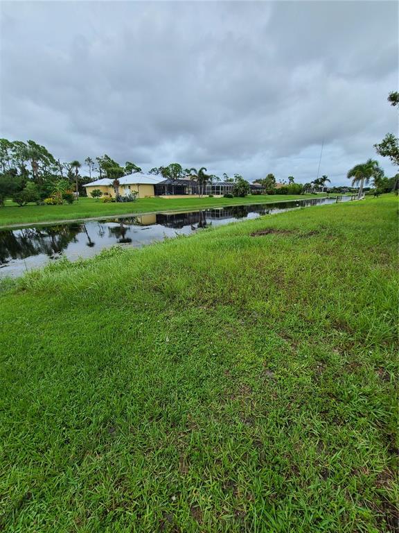 A grassy lawn slopes down to a canal with a house visible in the background — 254 LONG MEADOW LANE, ROTONDA WEST, FL