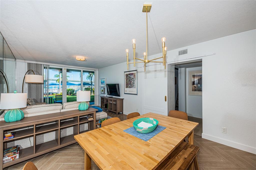 A dining area with a wooden table and chandelier opens into a living room with patio views — 5901 BAHIA DEL MAR CIRCLE UNIT 122, ST PETERSBURG, FL