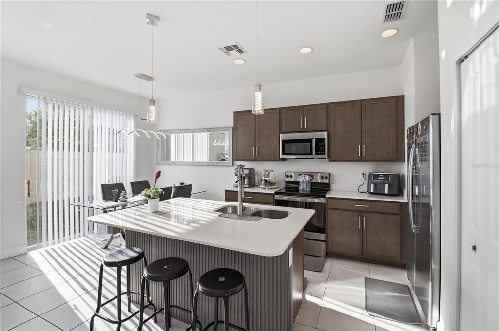 A modern kitchen features a white island with bar stools, dark cabinets, and stainless appliances — 1375 CAPTIVA COVE, SANFORD, FL