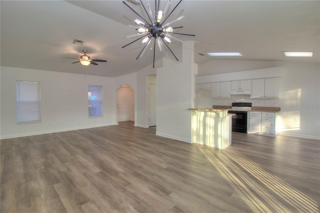 An open-concept living room and kitchen featuring wood-look flooring and a modern sputnik chandelier — 26 PECAN PASS TRAIL, OCALA, FL