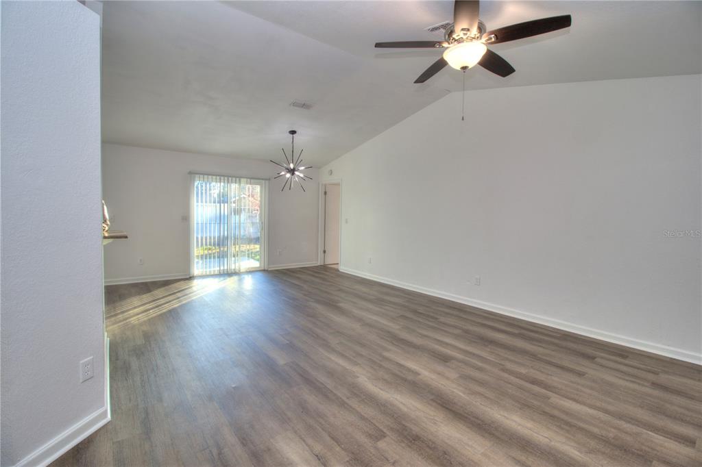 An empty living room features wood-look flooring, a vaulted ceiling, a ceiling fan, and sliding doors — 26 PECAN PASS TRAIL, OCALA, FL